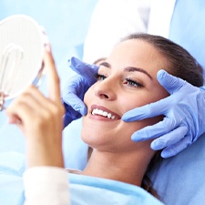 Woman smiling into hand mirror after dental emergency